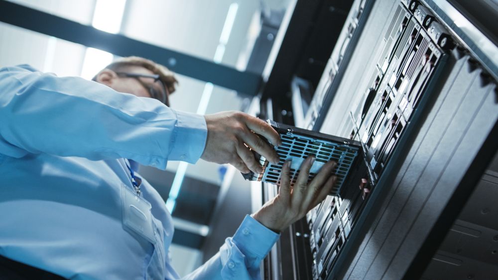 Long Angle Shot In Fully Working Data Center of IT Engineer Installing Hard Drive into Server Rack.