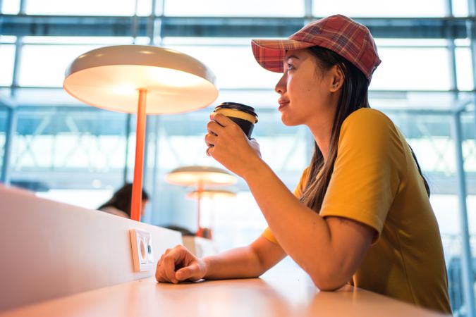 Asian woman drinking coffee at table under lighting lamp