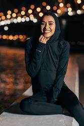 Woman in dark sportswear sitting on riverbank at night by lit bridge