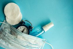 Clock, cotton, spray and facemask on blue pastel background
