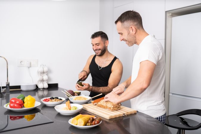Smiling male couple preparing vegetables and cutting bread for lunch