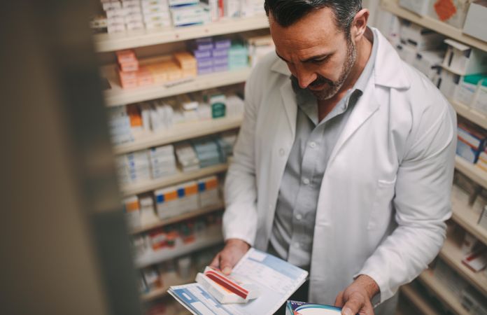 Pharmacist holding prescription and reading content on medicine box in pharmacy