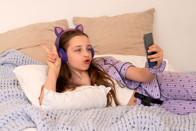 Girl making playful face while using smartphone in bed.
