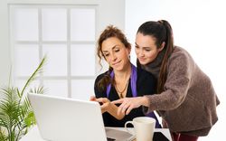two women point to laptop screen talking about work in