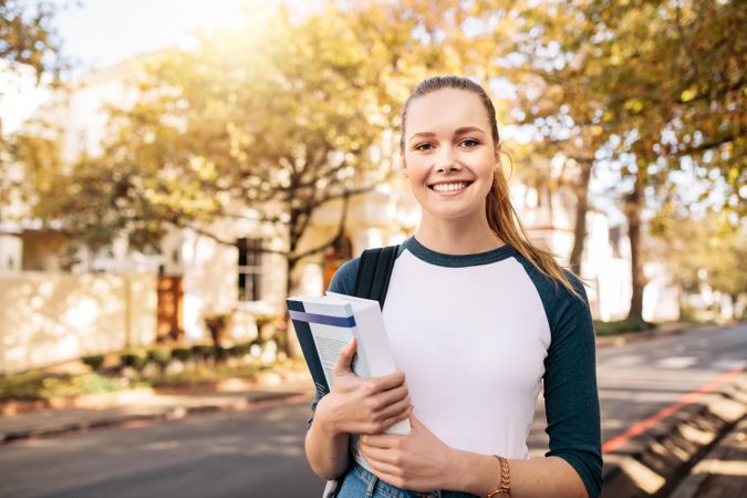 Youthful white female holding textbooks and smiling at camera