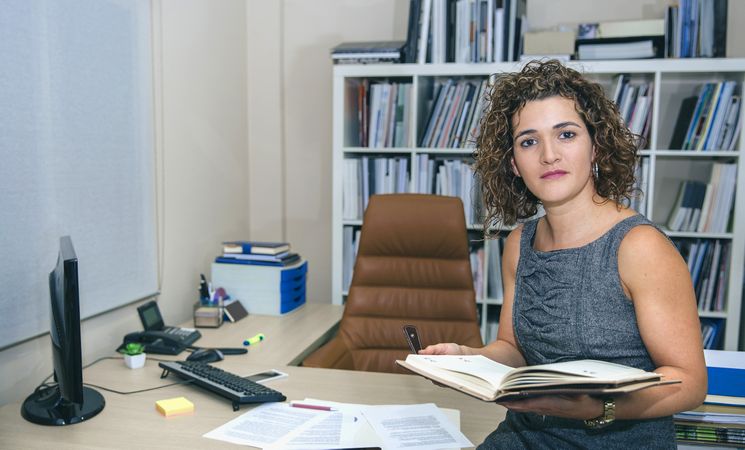 Businesswoman looking up from notebook in office with bookcase