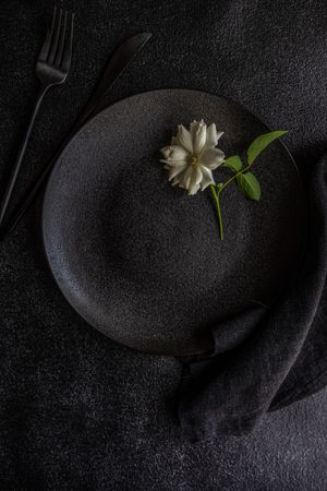 Top view of minimalistic table setting with single rose on dark plate