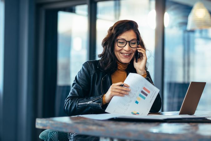 Woman tech executive talking on phone while going through  paperwork at work place