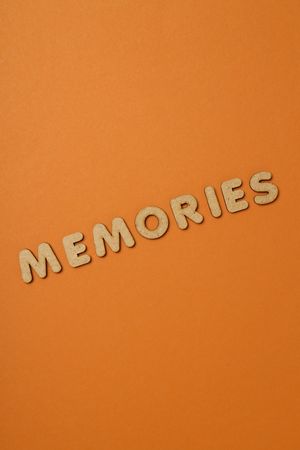 The word “Memories” written in cork in center of dusty orange background, vertical with copy space