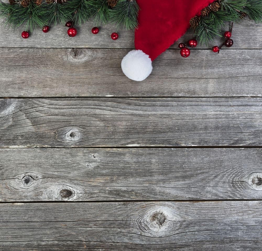 Merry Christmas or happy New Year background with fir tip branches and red Santa Claus cap on rustic wood