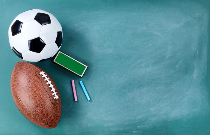 American football and soccer ball on cleaned chalkboard with writing materials