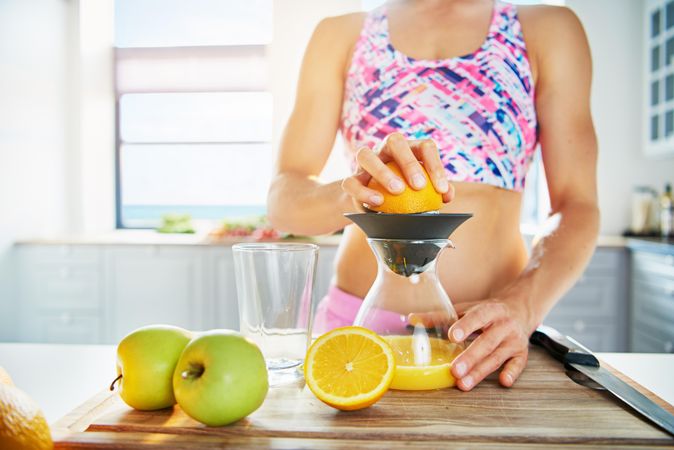 Woman in athletic gear squeezing oranges at cutting board
