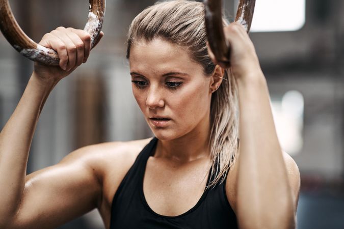 Healthy serious woman holding onto gymnastic rings at the gym