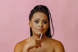 Surprised Black woman holding lip gloss while looking up