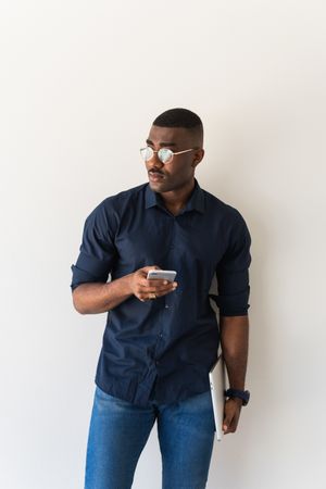 Thoughtful Black man with phone and laptop near white wall