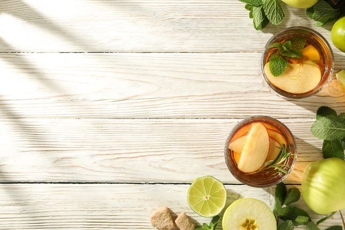 Glasses with apple cider, mint branches and apples on light wooden background, space for text