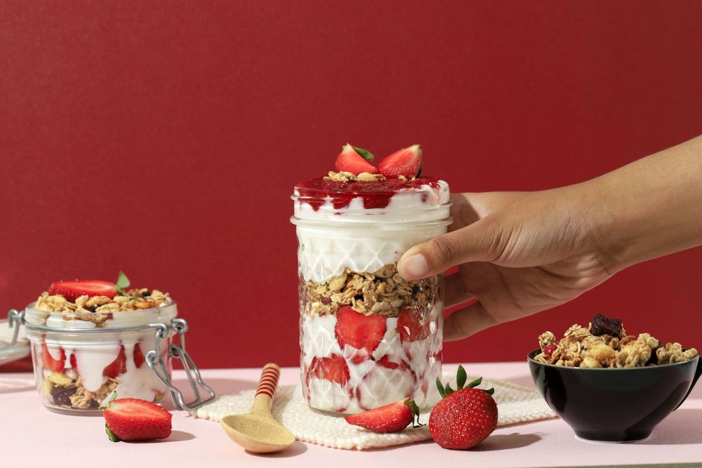Hand reaching for very parfait with layered granola, fruit and yogurt