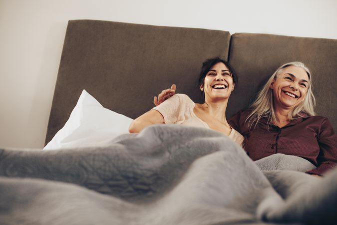 Happy daughter and mother lying on bed at home and laughing together