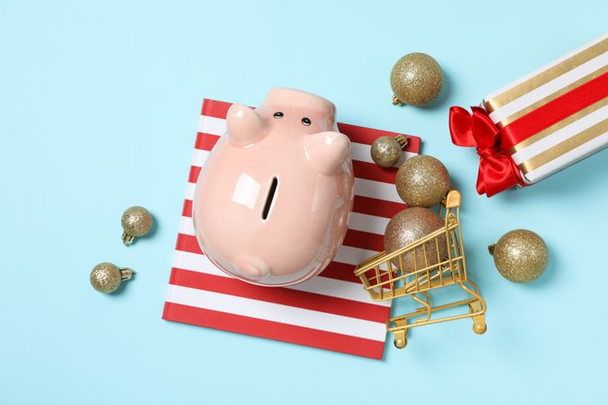 Piggy bank, gift boxes and trolley with balls on blue background, top view