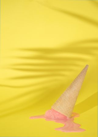 Upside-down cone with pink scoop of melting ice cream on yellow background