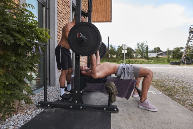 Black man spotting friend lifting barbell on street