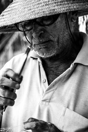 Close-up photo of an older man wearing eye glasses and hat in grayscale