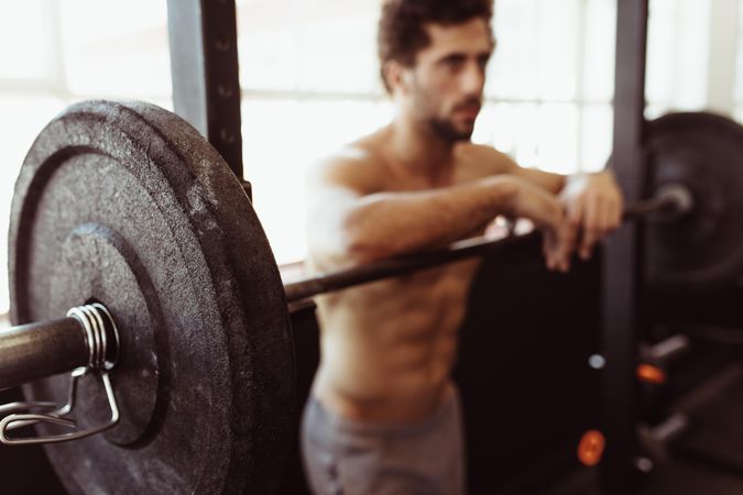 Muscular man leaning over barbell after training in gym