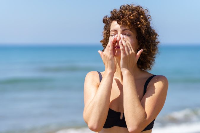 Woman smearing sunblock cream on face near sea