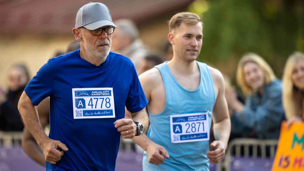 Portrait of a Mature Male Jogger Running in a City Marathon and Being Cheered for by the Audience.