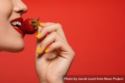 Female biting into a strawberry against a red background 5kEYAb