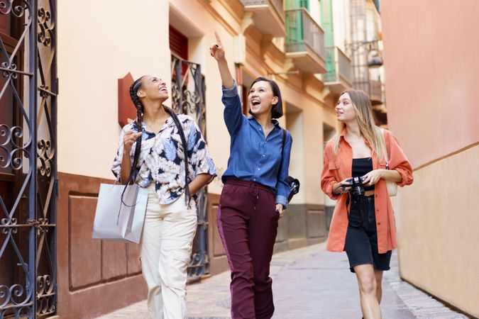 Three happy women walking down narrow lane pointing up