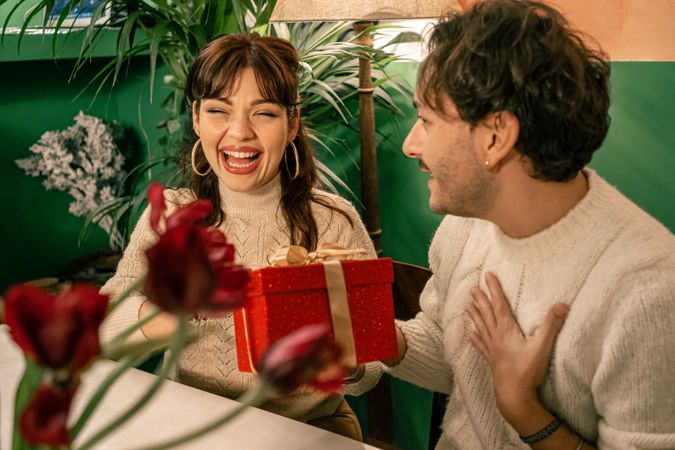 Joyful woman receiving a Christmas gift from her partner during a celebration.