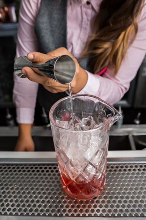 Cropped image of bartender pouring spirits to a stirring glass