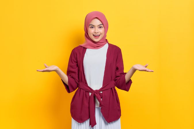 Woman in red headscarf smiling with both hands up, questioning