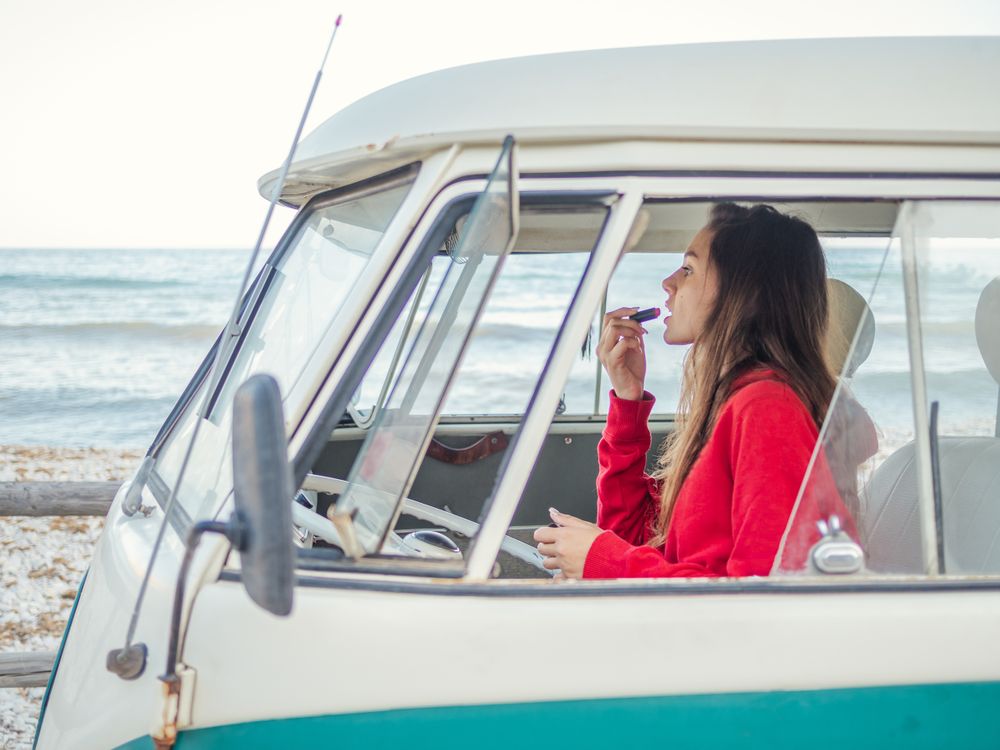 Woman painting lips looking in front mirror of car
