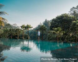 Man standing beside swimming pool surrounded by tropical trees 5oBP10