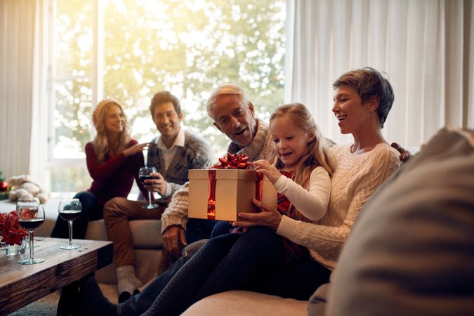 Little girl sitting in living room with family opening christmas gifts