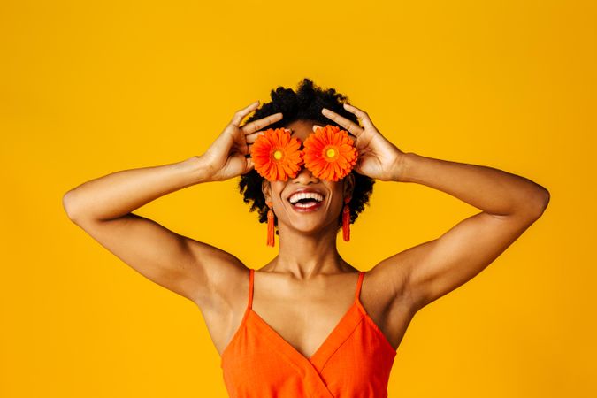Happy Black woman holding two flowers over her eyes
