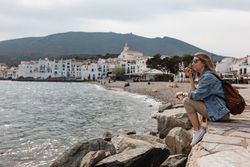 Young woman on smart phone speaker sitting on jetty near the beach