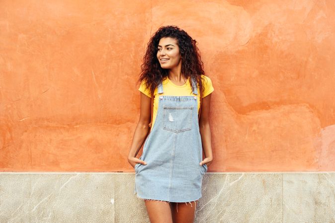 Arab woman with curly hairstyle looking to her left side while leaning on orange wall
