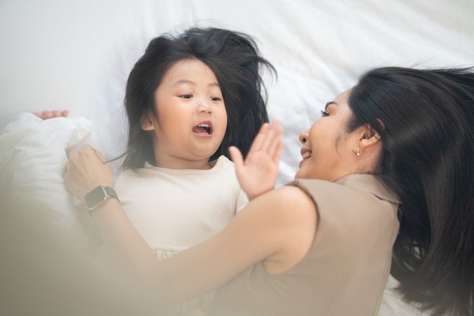 Top view of Asian mother and daughter cuddle and talking on bed.