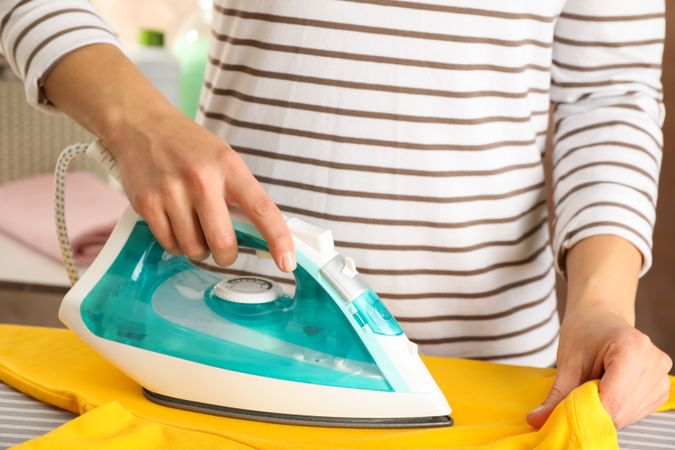 Young woman ironing yellow t-shirt, close up