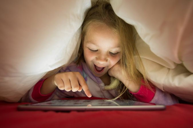Girl using tablet under blanket