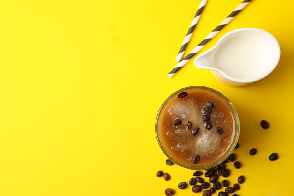 Glass of ice coffee on yellow background. Fresh drink