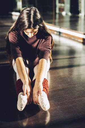 Ballerina sitting on floor in sunlight and bending forward warming up muscles.
