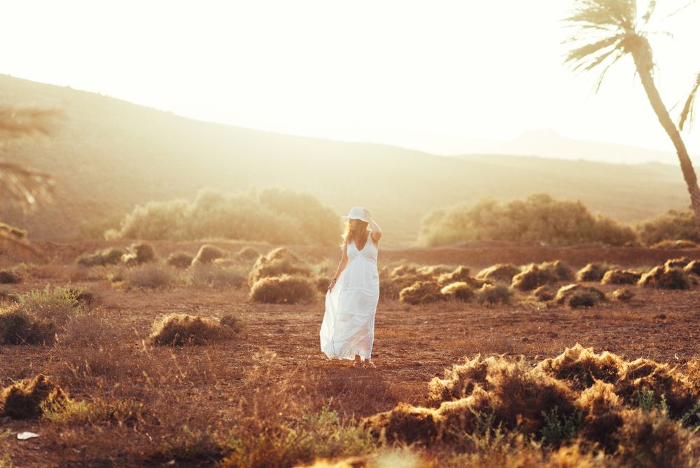Woman in white dress in dry field in sunlight