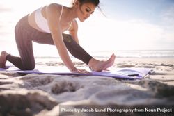 Woman doing leg stretches on the beach 4jvnX4