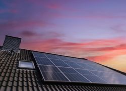Solar panels producing clean energy on a roof of a residential house during sunset.