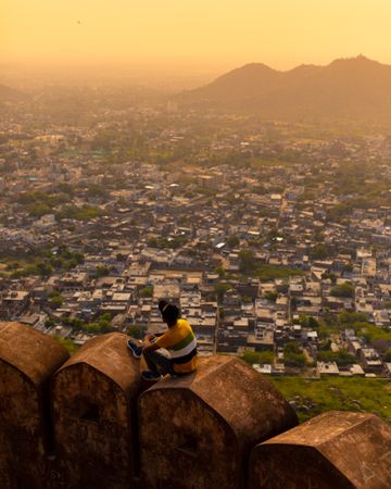 High angle view of a young man sitting on brown wall with Mumbai cityscape in the background at sunset