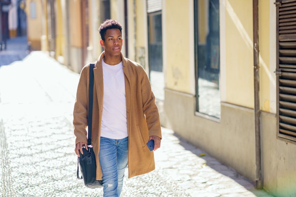 Cuban male strolling down street with leather bag and phone